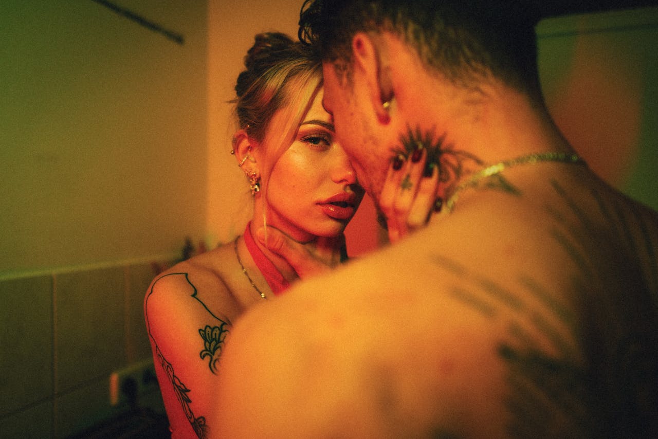 A close, intimate moment between a tattooed couple, captured in warm lighting.
